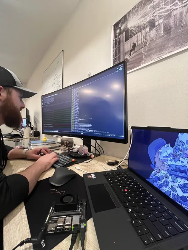 An engineer at a desk, a terminal running on the monitor and a single-board computer wired up beside the laptop
